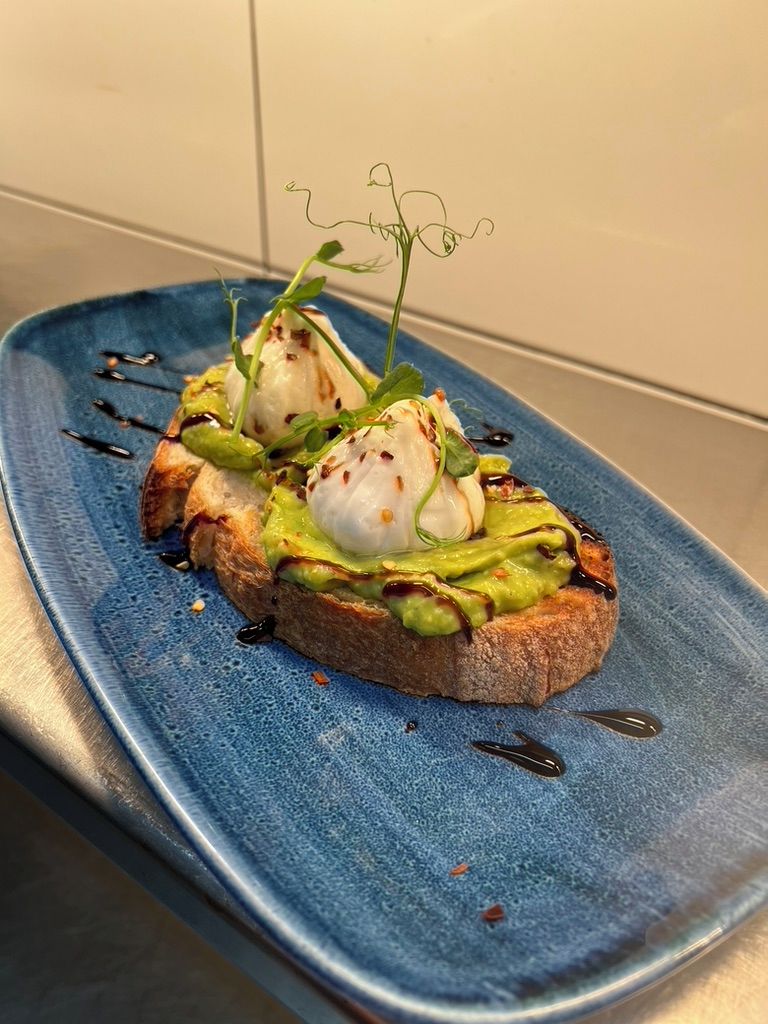 Une assiette bleue avec deux œufs pochés sur des toasts, de l’avocat et une garniture.