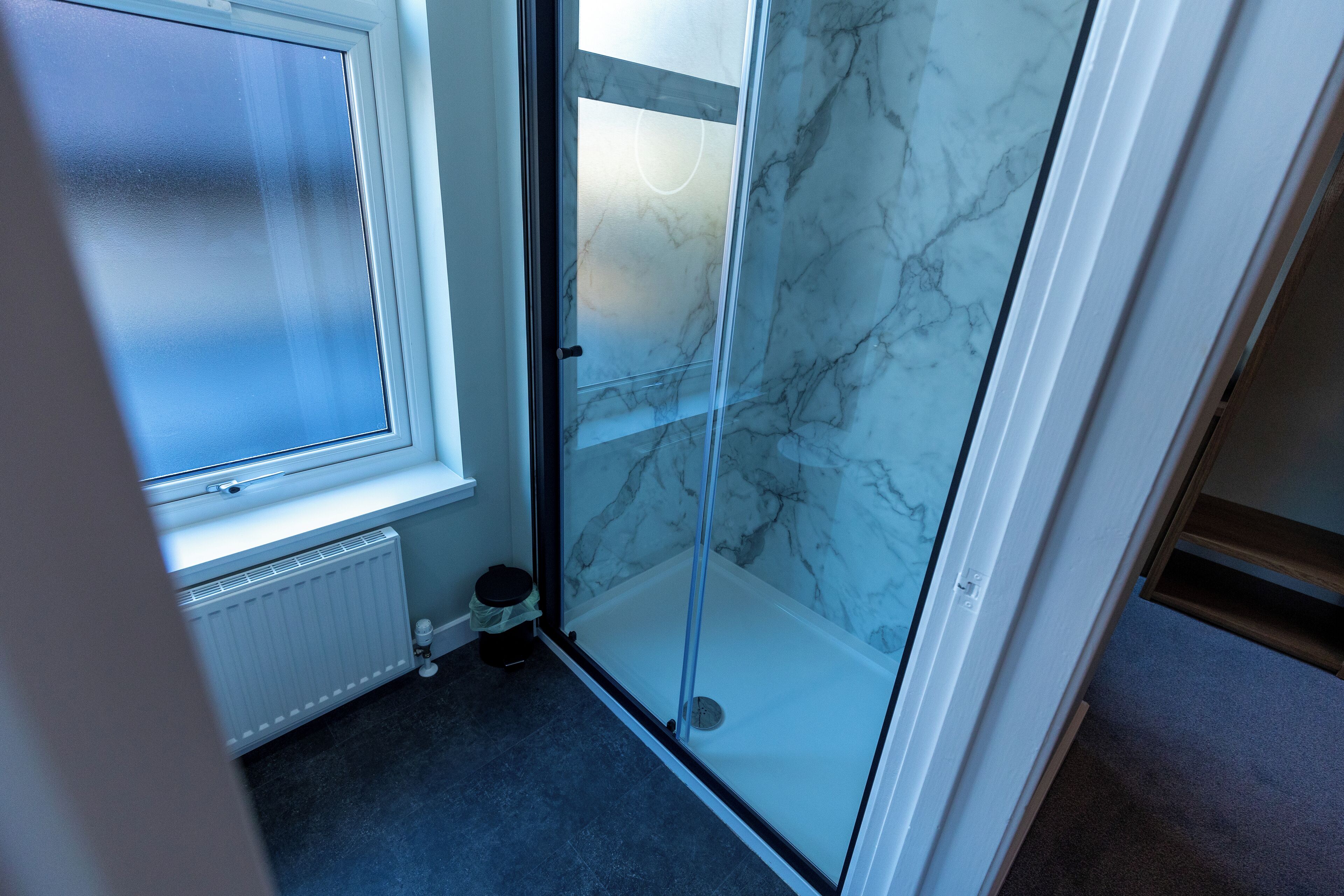 Een badkamer met een douchecabine van glas, een witte radiator en een raam.