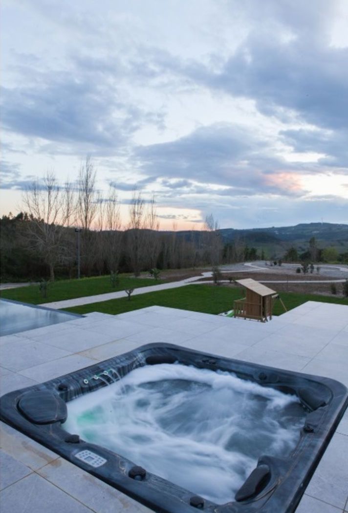 A hot tub with a view of a landscaped area and a wooden structure in the background.
