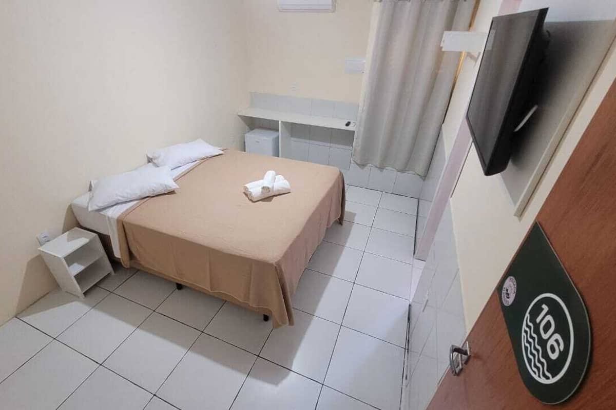 A small, clean room with a bed, a TV, and a shower area.