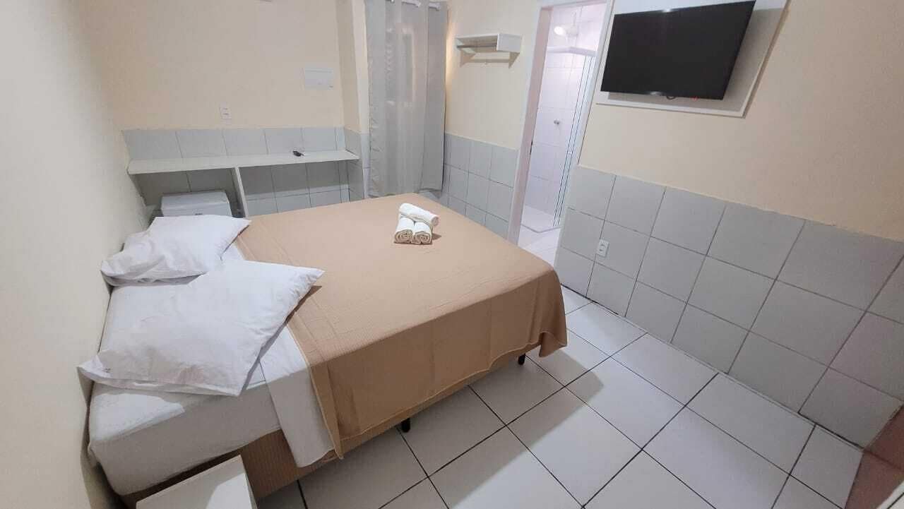 A hotel room with a bed, a small desk, a TV, and a shower area.