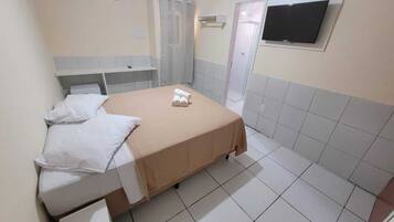 A hotel room with a bed, a small desk, a TV, and a shower area.