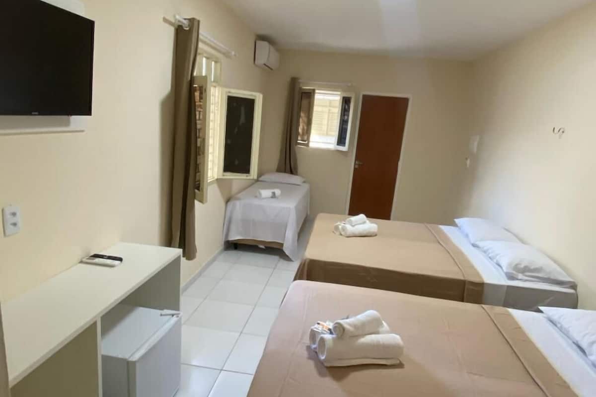 A hotel room with two single beds, a desk with a chair, a television mounted on the wall, and a window with curtains.