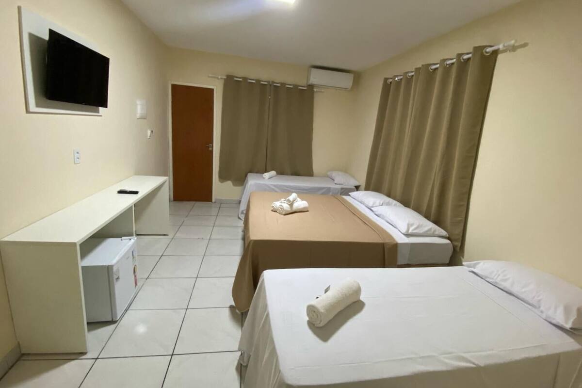 A hotel room with two beds, a desk, a TV, and an air conditioning unit.