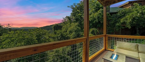 A wooden deck with a glass railing, a fire pit, and a sofa.