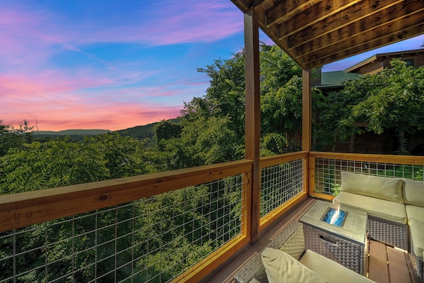 A wooden deck with a glass railing, a fire pit, and a sofa.