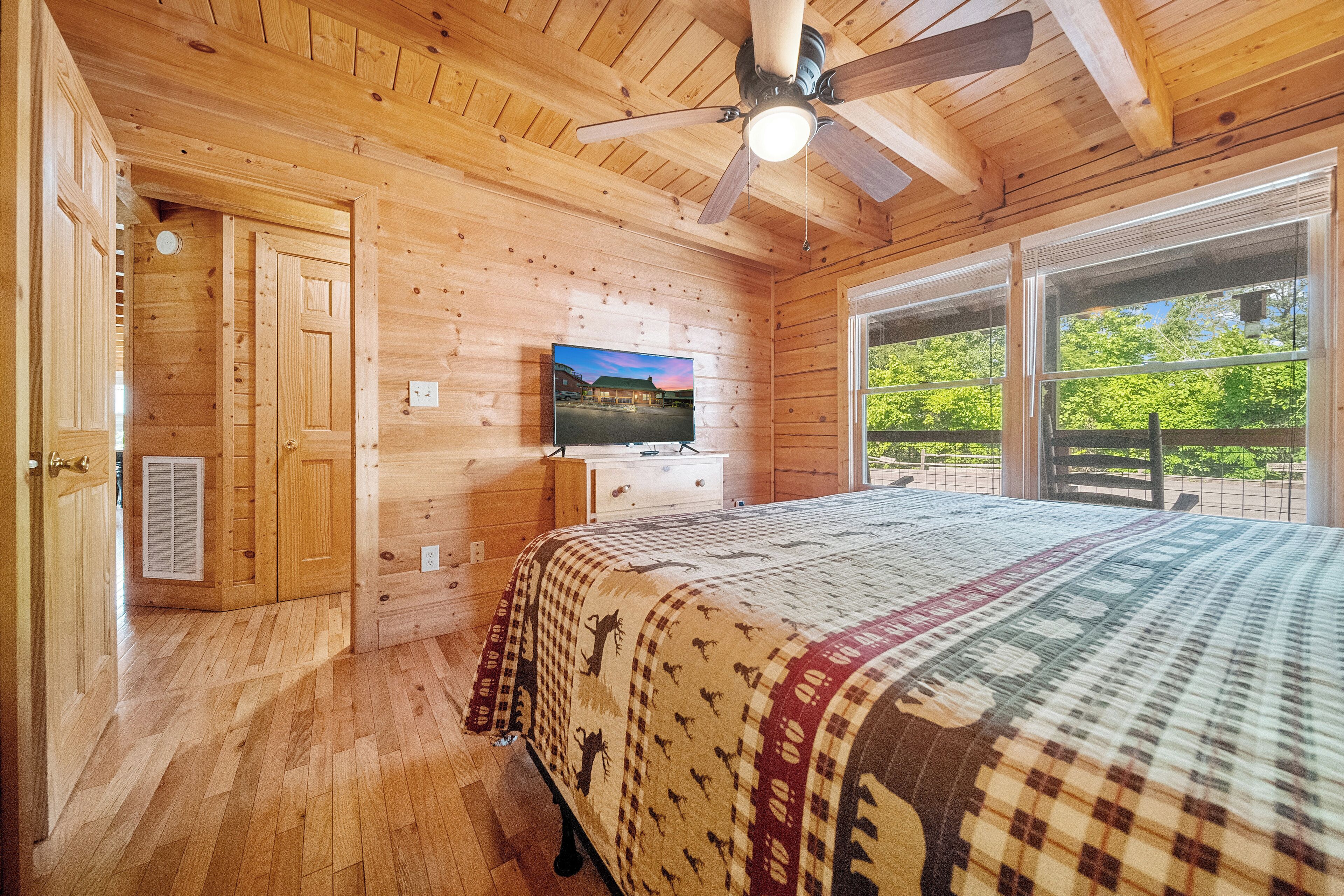 Habitación de cabaña de madera con cama, televisor y ventana con vistas a la vegetación.