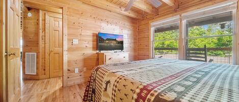 Habitación de cabaña de madera con cama, televisor y ventana con vistas a la vegetación.