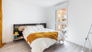 Un dormitorio moderno con cama, mesita de noche, planta en maceta y ventana con vista a un edificio.