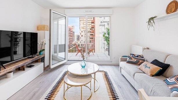 Una sala de estar moderna con un ventanal grande, un televisor de pantalla plana, una mesa de centro redonda y un sofá con almohadones decorativos.