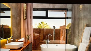 A modern bathroom with a freestanding bathtub, a vanity with a sink, and a large window offering a view of palm trees. - Villa Baidane Avec sa Somptueuse vue sur L'atlas (sidi abd alla ghiat)