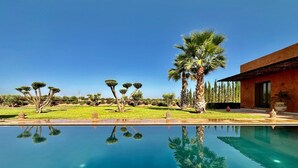 A swimming pool with clear blue water, surrounded by a well-maintained lawn and palm trees. - Villa Baidane Avec sa Somptueuse vue sur L'atlas (sidi abd alla ghiat)