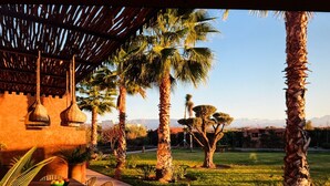A patio with a table and chairs, surrounded by palm trees and a view of mountains. - Villa Baidane Avec sa Somptueuse vue sur L'atlas (sidi abd alla ghiat)