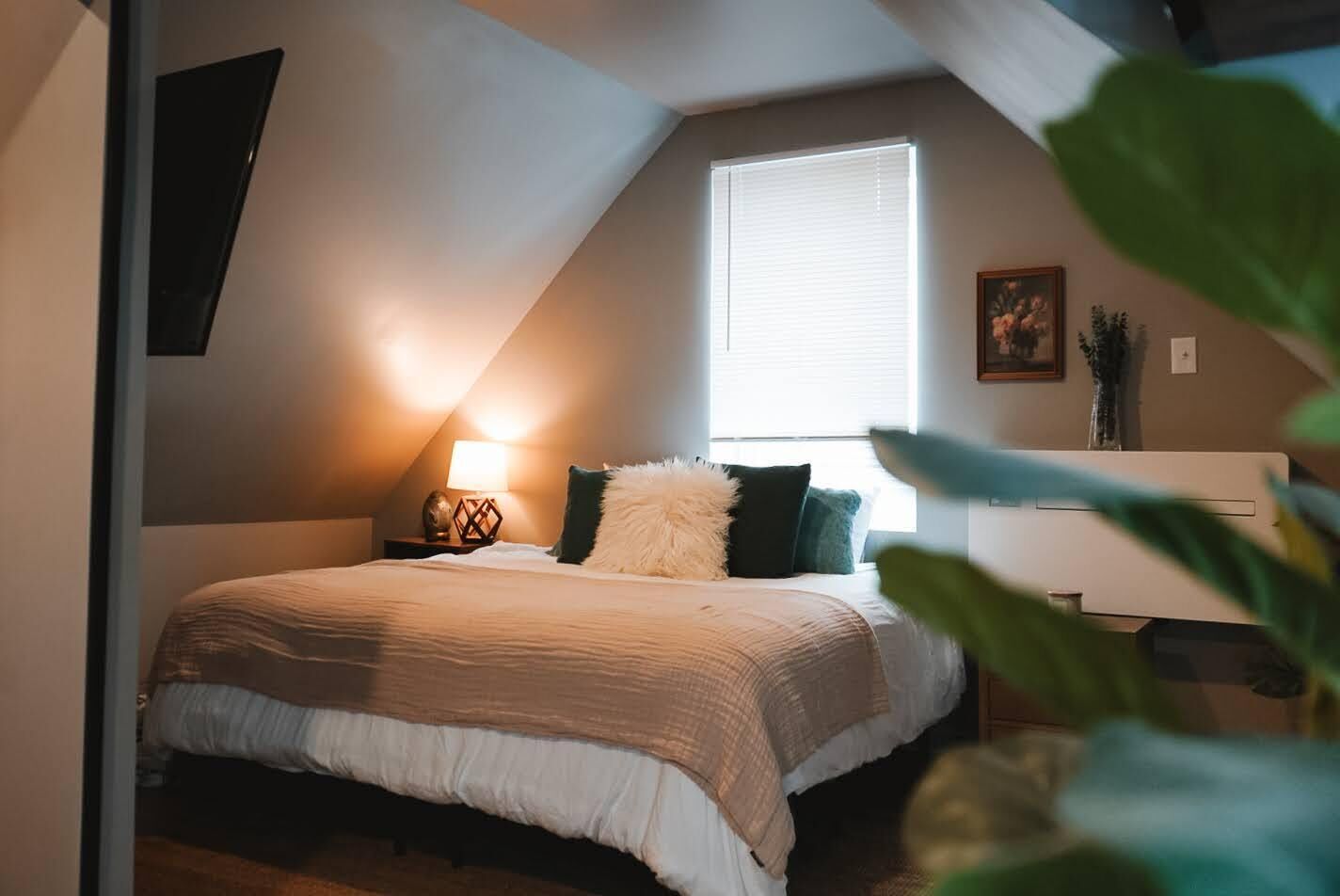 A bedroom with a bed, a nightstand, a lamp, and a window.