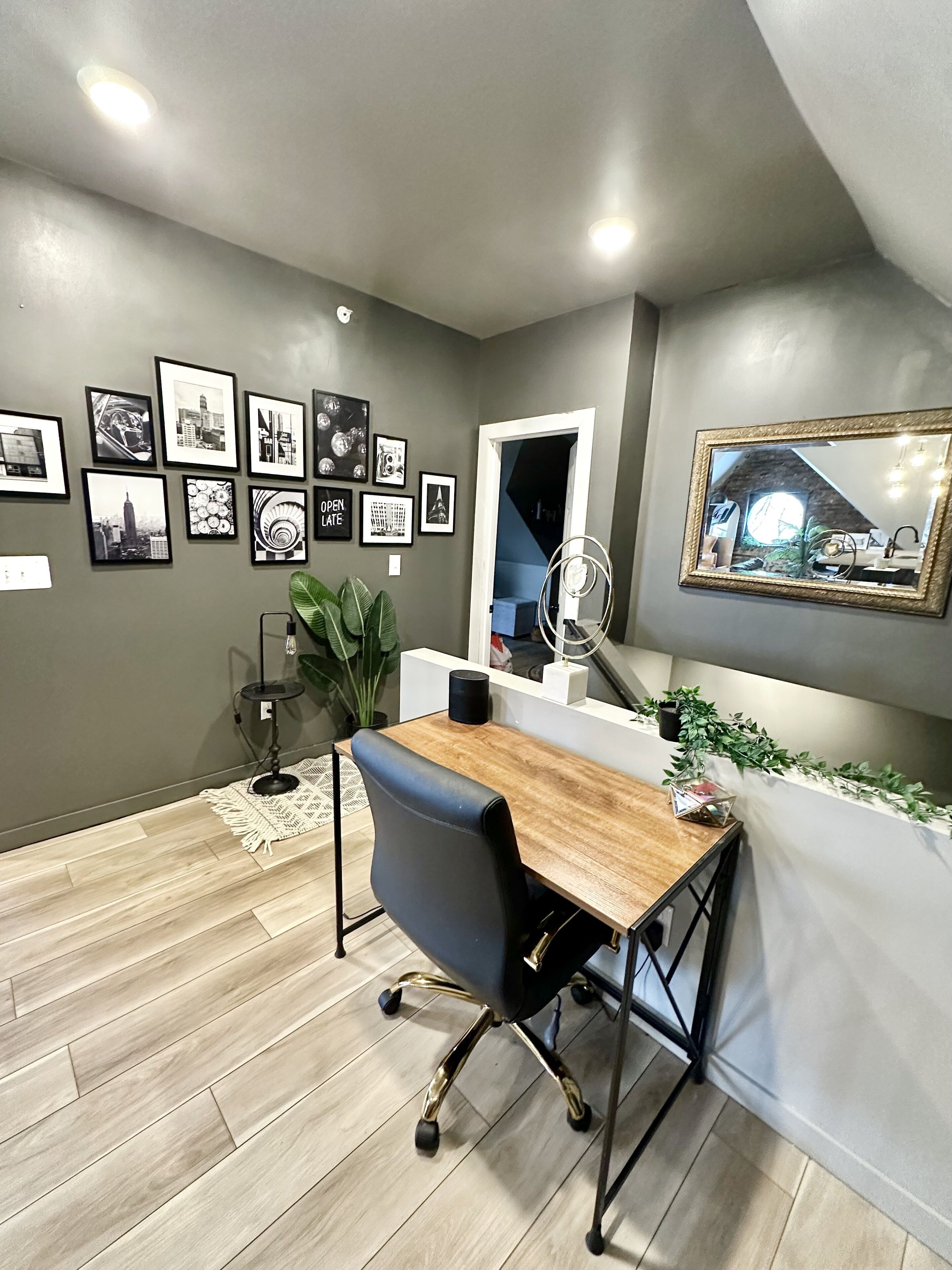 A modern office space with a wooden desk, black office chair, and a wall adorned with framed pictures.
