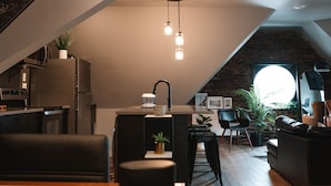 Un loft moderne comprenant une cuisine, un coin repas et un espace de vie. Il est doté d’un îlot de cuisine, d’une table à manger et d’un canapé en cuir noir.