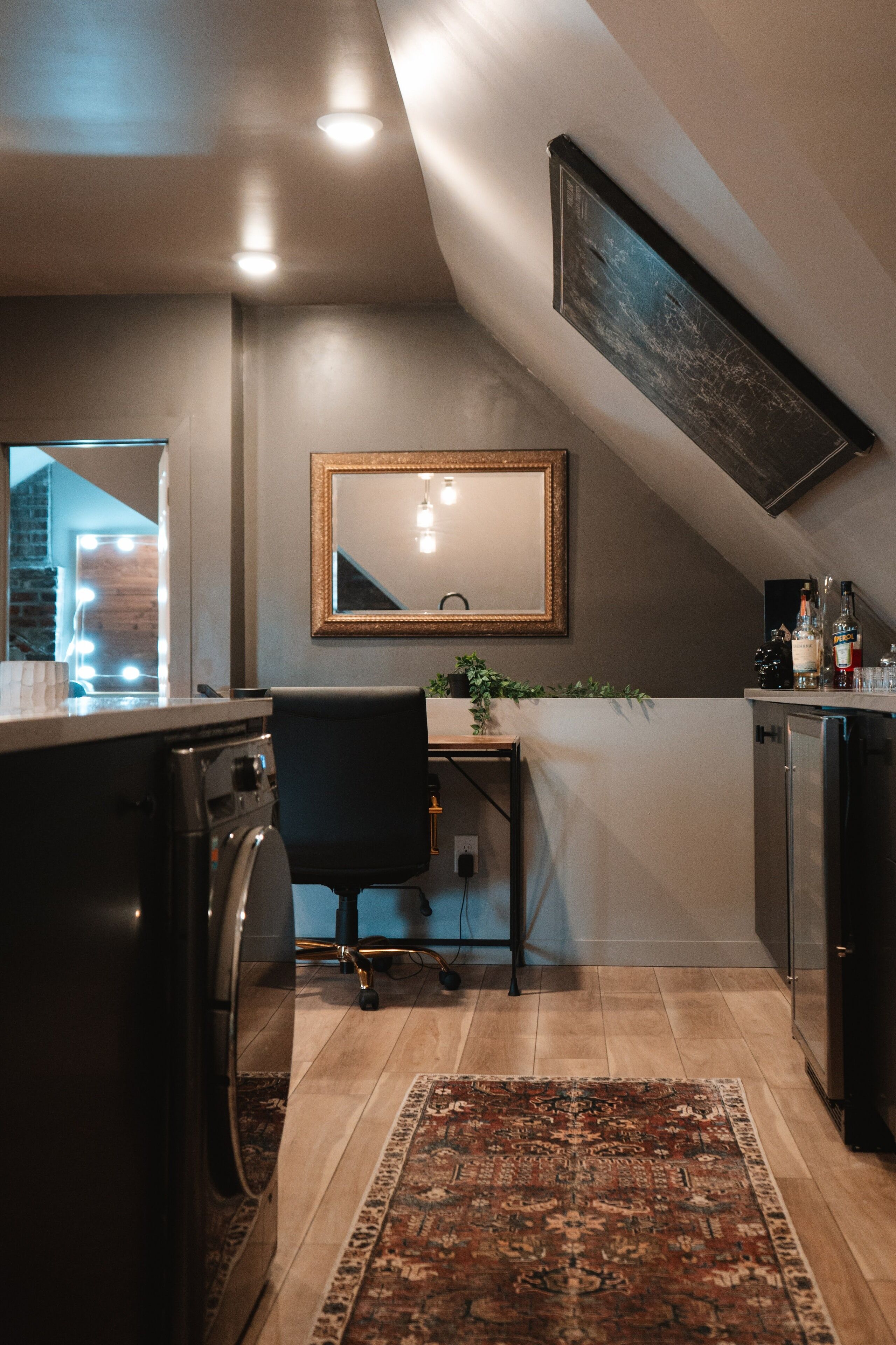 A compact kitchen with a washing machine, a desk, and a mirror.