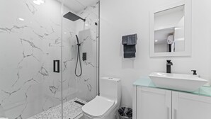 A modern bathroom with a glass-enclosed shower, white marble walls, a white toilet, a glass sink, and a mirror above the sink. - XL Luxury Room. Luxurious studio retreat with sleek designs. (Miami)