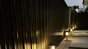 A modern outdoor pathway with a metal fence and gravel, illuminated by ground lights. - XL Luxury Room. Luxurious studio retreat with sleek designs. (Miami)