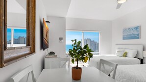 A modern hotel room with a large window, a dining area with a table and chairs, and a bed with white bedding. - Modern Studio | Gulf Views | Luau I 7101 | Sandestin (Miramar Beach)