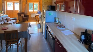 Une cuisine spacieuse avec des poutres en bois, un coin repas avec une table et des chaises, et une vue sur le salon par une porte ouverte.