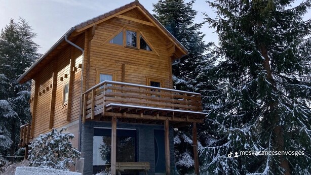 Une cabane en bois dotée d’un balcon, entourée d’arbres couverts de neige.