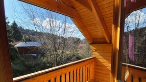 Un balcon en bois doté d’un plancher à carreaux et offrant une vue sur des arbres et une maison au loin.