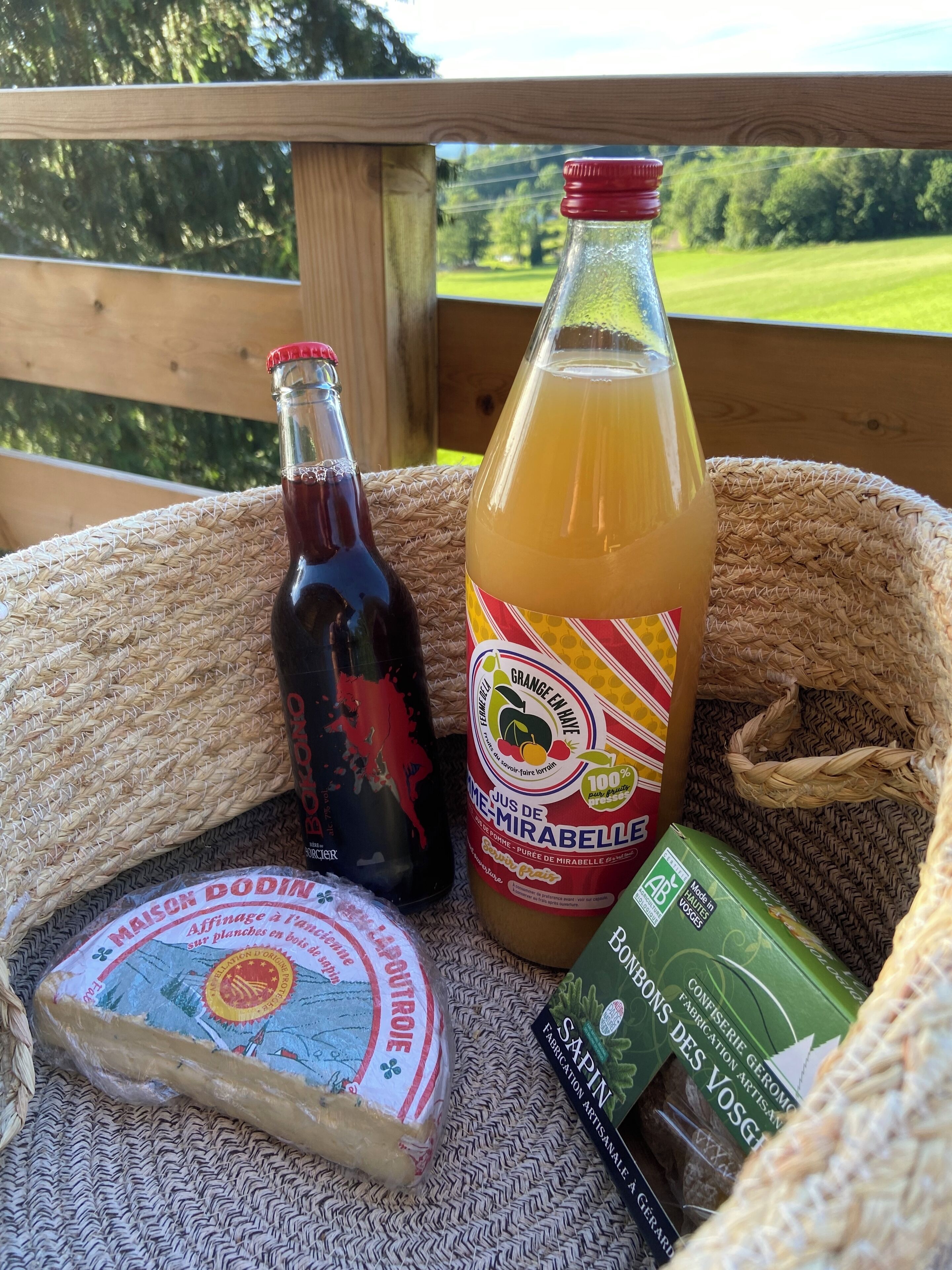 Ein Korankorb mit einer Flasche Grange En Hiver, einer Flasche Rotwein, einer Packung Gouda-Käse und einer Schachtel Ahornsirup-Honig.