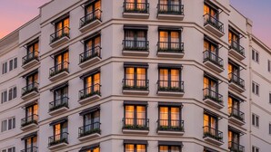 Un hotel de varios pisos con un diseño arquitectónico clásico, que cuenta con balcones con plantas, grandes entradas en arco y señalización iluminada.