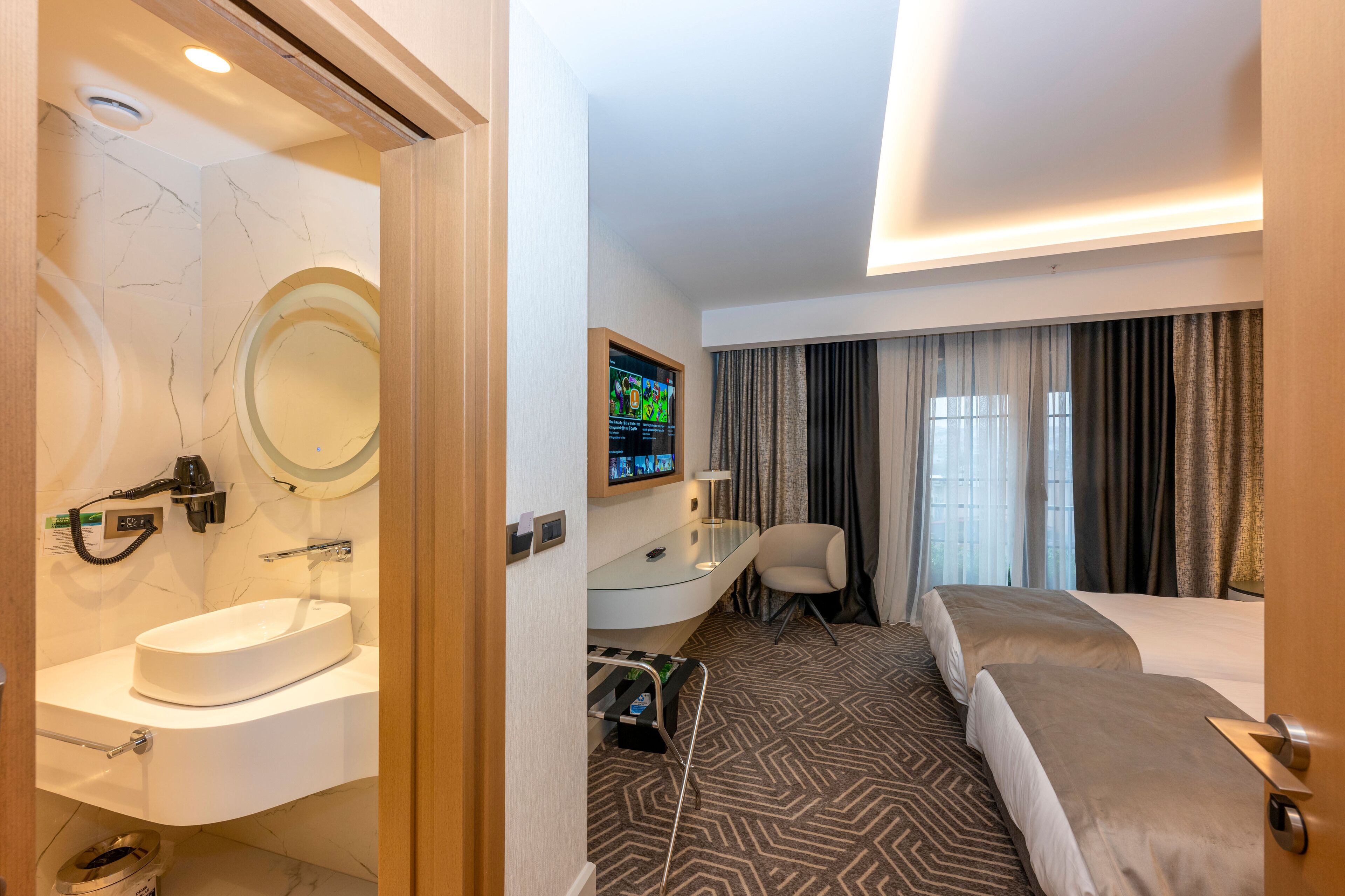 Une chambre d’hôtel avec une salle de bain en marbre, un bureau avec un ordinateur, un lit et une télévision.