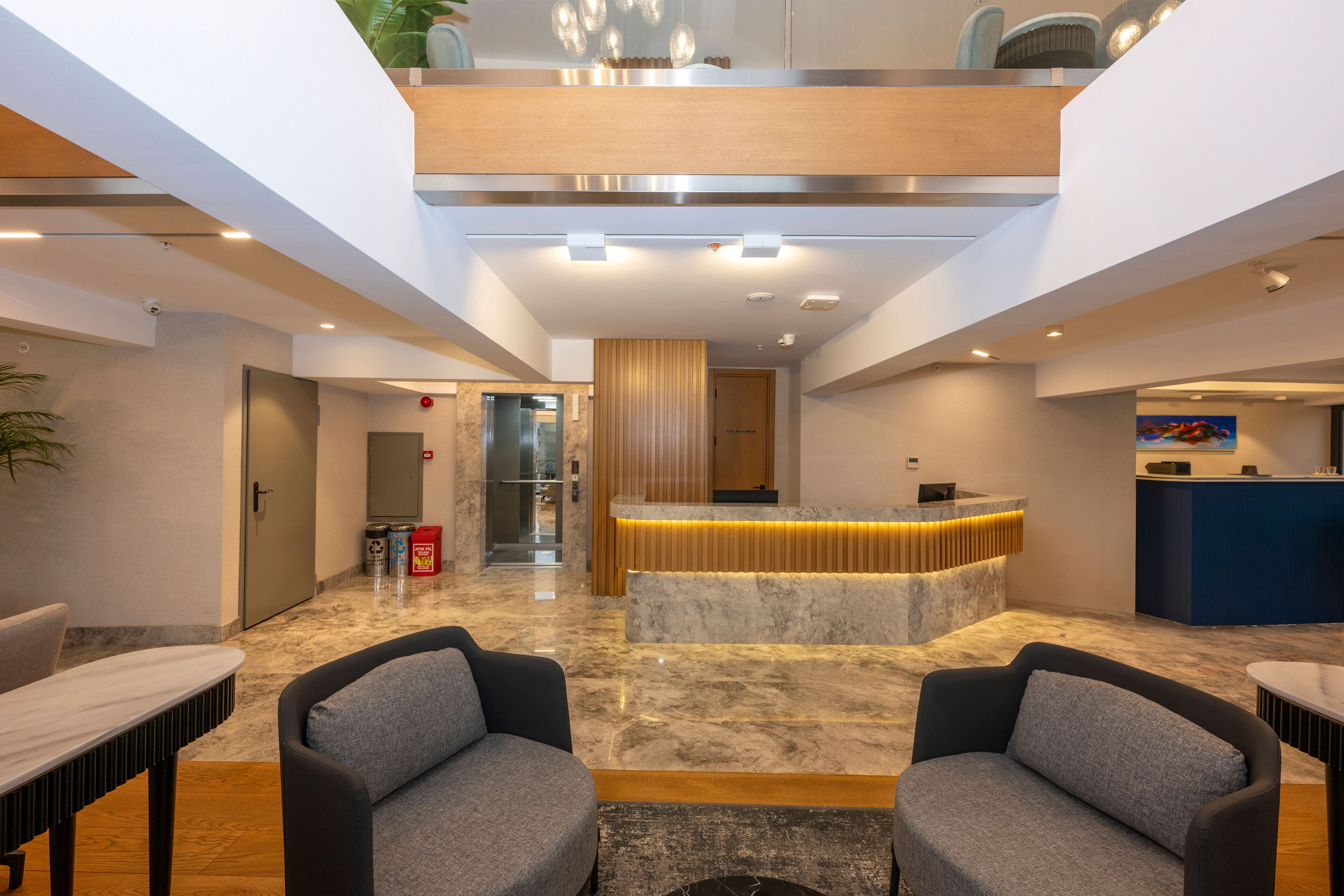 A modern lobby with a reception desk, seating area, and a high ceiling with recessed lighting.