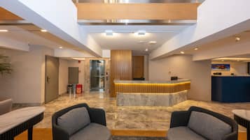A modern lobby with a reception desk, seating area, and a high ceiling with recessed lighting.