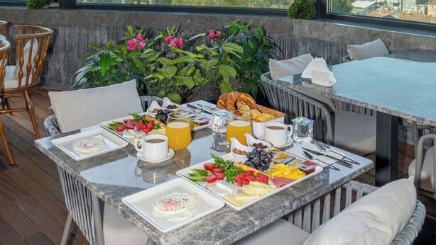 Zona de comedor en la azotea con una mesa lista para el desayuno, con vistas a un paisaje urbano.