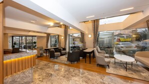 Un moderno vestíbulo de hotel con mostrador de recepción, zona de estar y grandes ventanales que ofrecen vistas a la ciudad.