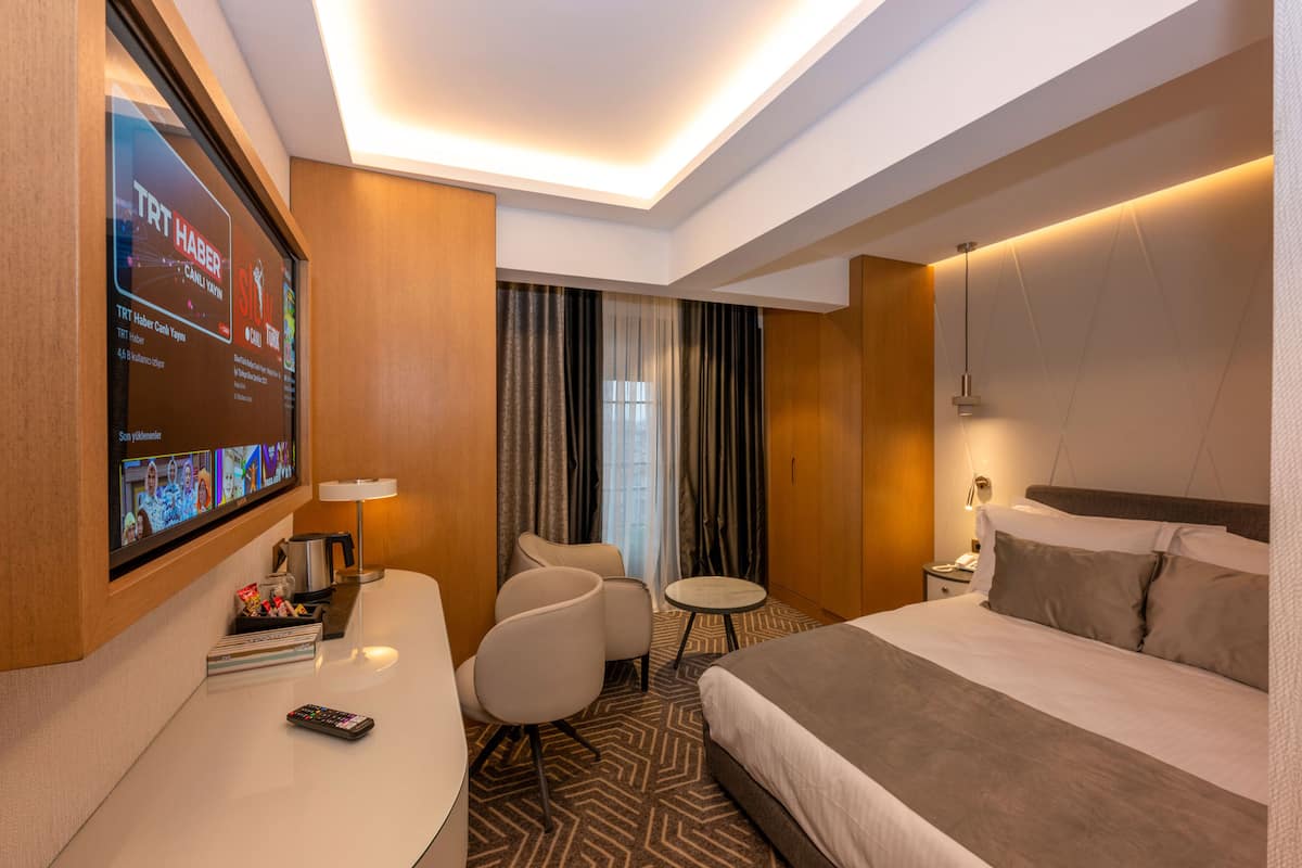 Habitación de hotel con cama, escritorio con televisor, silla, una mesita y mesita de noche con lámpara.