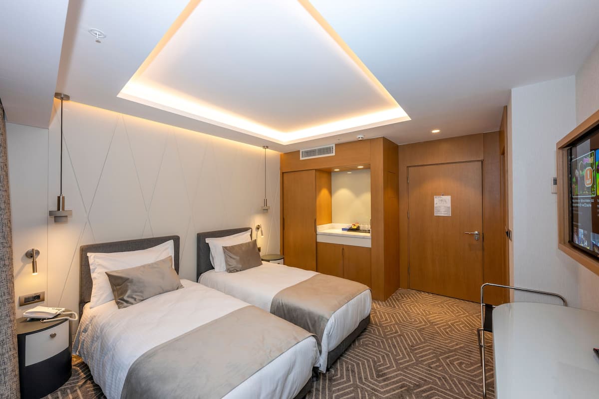 Una habitación de hotel con dos camas, un escritorio, un espejo y una lámpara en el techo.