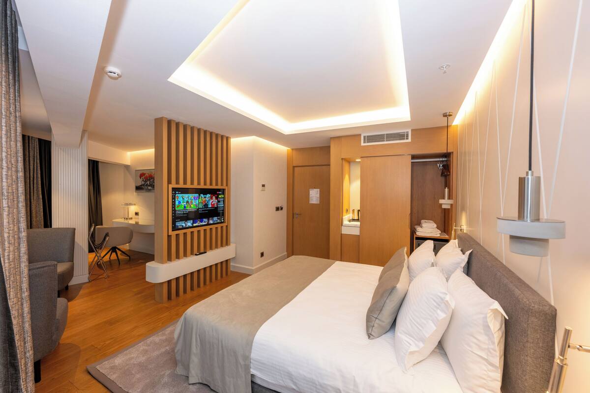 Una habitación de hotel moderna con una cama grande, un televisor montado en la pared, un escritorio y un armario.