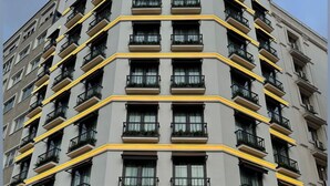 Un hotel de varios pisos con diseño moderno, que cuenta con balcones con plantas, una entrada destacada con fachada de vidrio y el nombre "BAVER HOTEL" exhibido sobre la entrada.