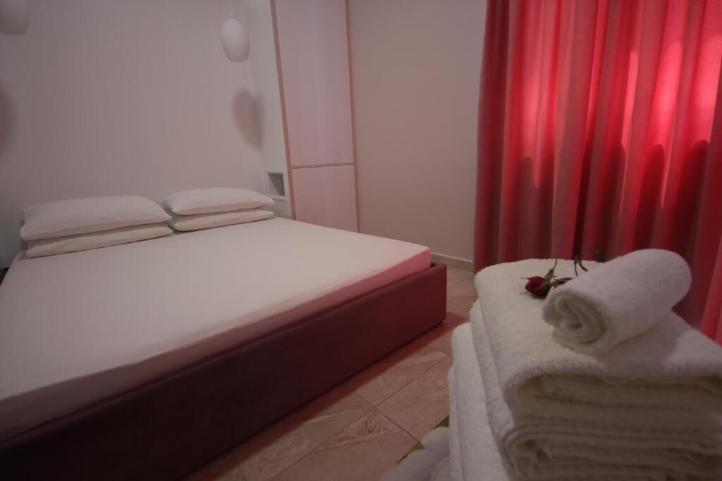 Een netjes opgemaakt bed met kussens, een opgerolde witte handdoek en een roos op een stapel handdoeken.