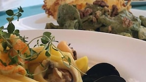 Una mesa de comedor con platos de pasta y vistas a una playa y palmeras al fondo.