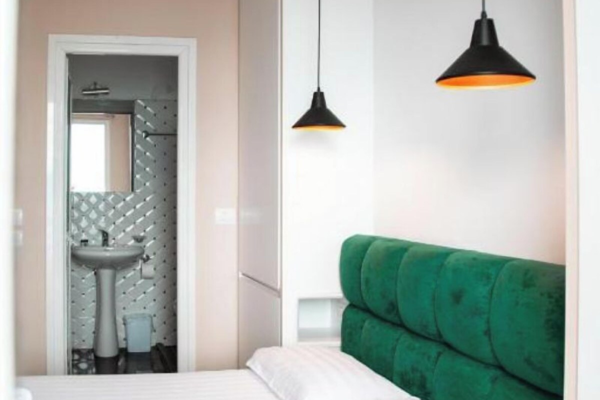 A bedroom with a green upholstered headboard, a white bedspread, and a hanging pendant light.