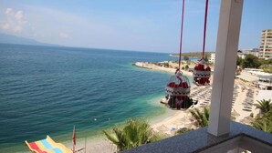 Vista de la playa con agua azul cristalina, una orilla arenosa y un edificio con una estructura roja y blanca.
