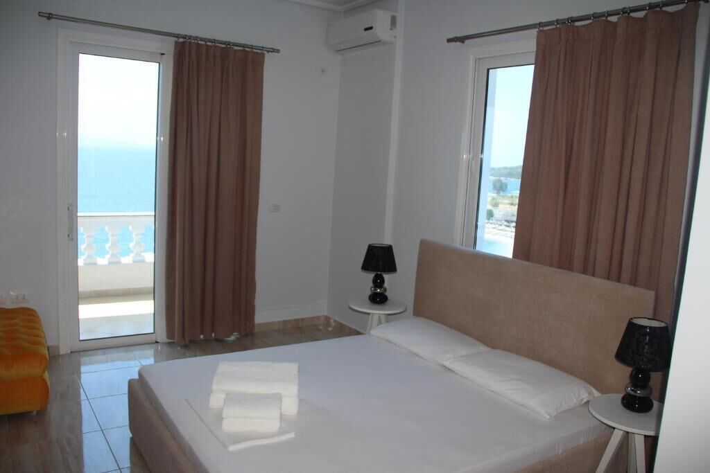 Una camera d'albergo con un letto, un tavolino con una lampada e vista sul mare dalla finestra.