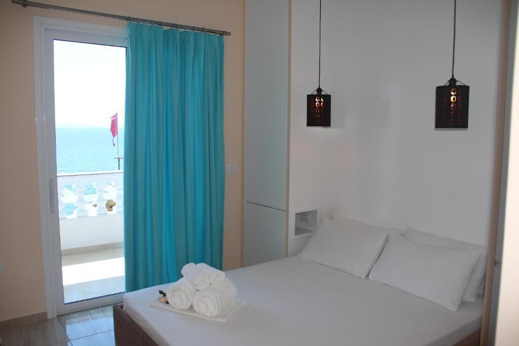 A hotel room with a bed, a window with a view of the sea, and a curtain.