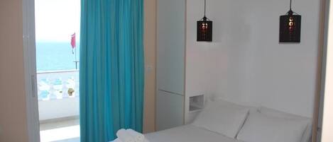 A hotel room with a bed, a window with a view of the sea, and a curtain.