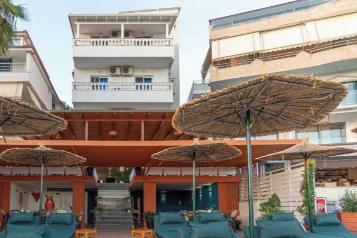 A pool area with lounge chairs and umbrellas, a staircase leading to upper floors, and a building with balconies.