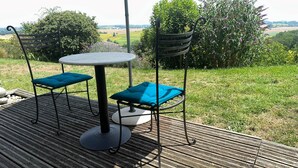 Een buitenpatio met een ronde tafel en twee stoelen, omringd door een houten terras en uitzicht op het buitengebied.