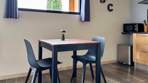 A modern kitchen with a dining area, a window with curtains, and a microwave. - Gite Bois & Cailloux (MONTGAILLARD LAURAGAIS)