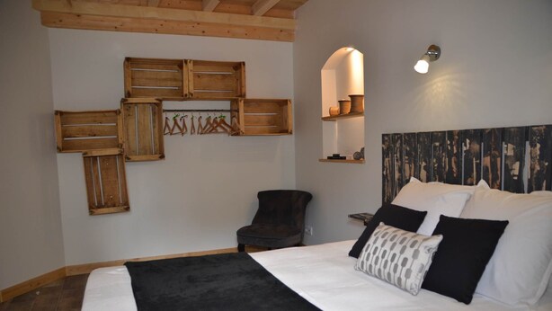 A bedroom with a bed, a chair, wooden wall decorations, and a wall-mounted shelf. - Gîte "La Cordonnerie (MONTGAILLARD LAURAGAIS)