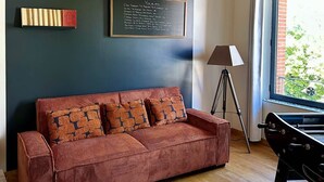 A room with a wooden ceiling, a dark blue wall, a red sofa with patterned cushions, a chalkboard menu, and a window with a view.